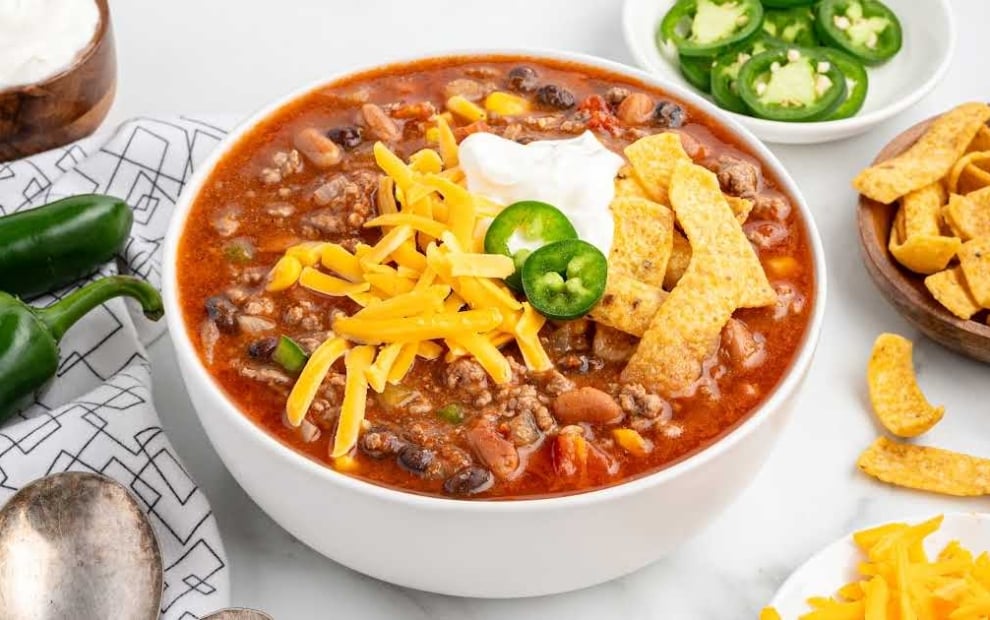 Overhead view of taco soup bowl with cheddar cheese, sour cream, jalapeño, and tortilla strips set against a background of the soup's surface.