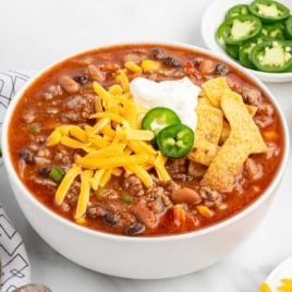 Overhead shot of taco soup in a bowl with toppings, placed next to fresh jalapeño slices, shredded cheese, and sour cream.