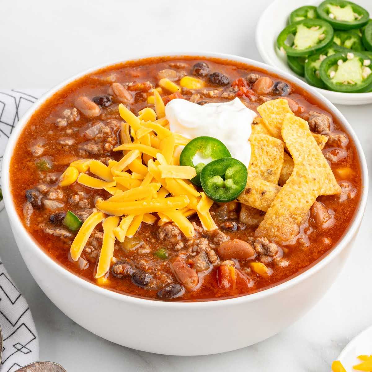 Overhead shot of taco soup in a bowl with toppings, placed next to fresh jalapeรฑo slices, shredded cheese, and sour cream.