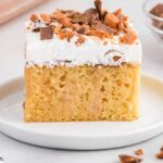 close up shot of a slice of Butterfinger Cake garnished with butterfinger candy bits on a plate