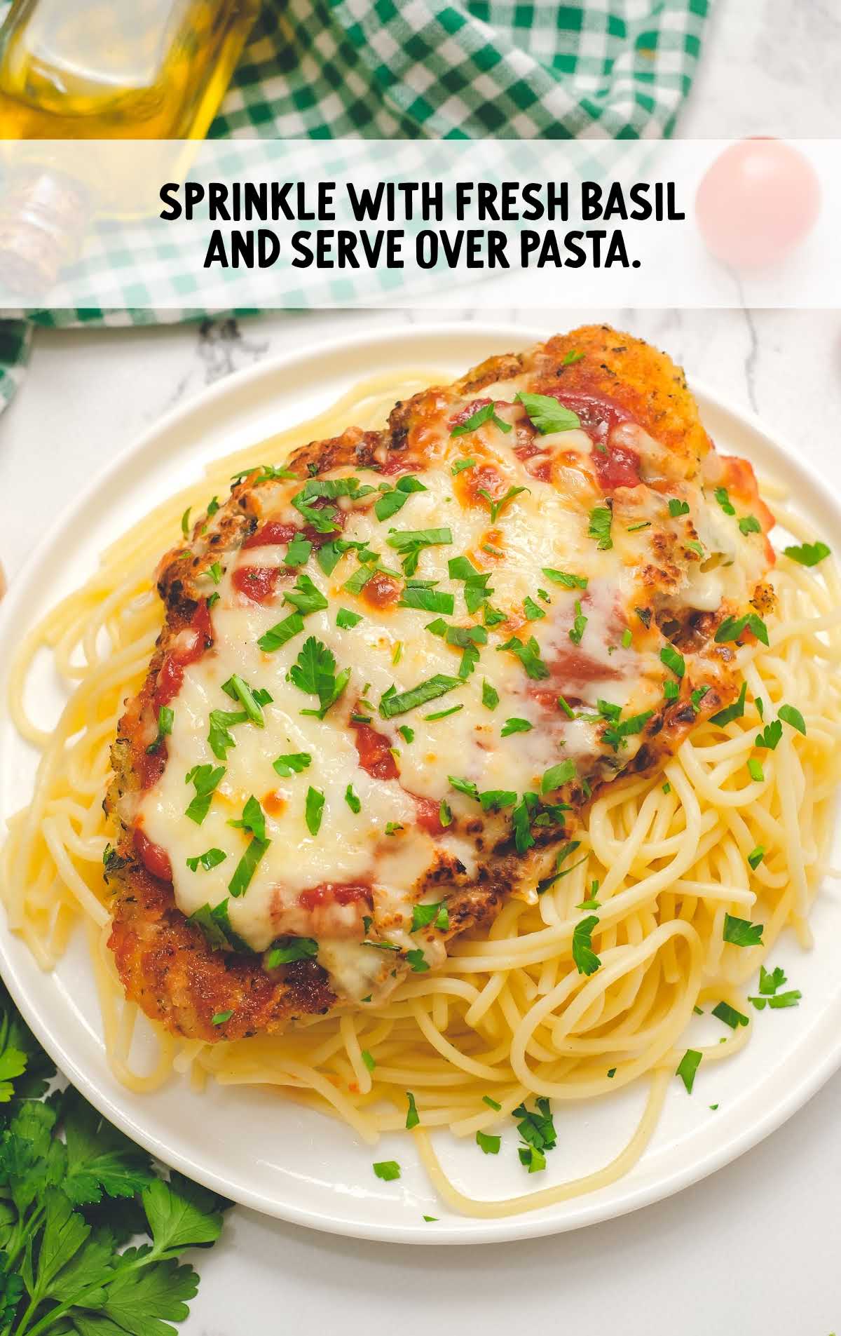 chicken topped with basil and served over spaghetti on a plate