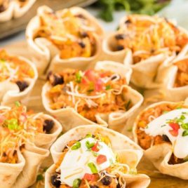 close up shot of Enchilada Cups filled and topped with cheese, sour cream, diced tomatoes, and diced green onions