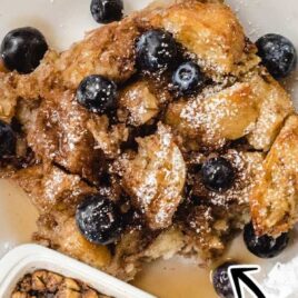 overhead shot of a baking dish full of French toast and a piece of French toast topped with blueberries on a plate