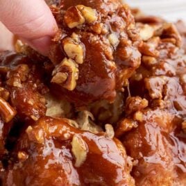 close up shot of Bread topped with glaze and pecans with a piece of bread being taken out