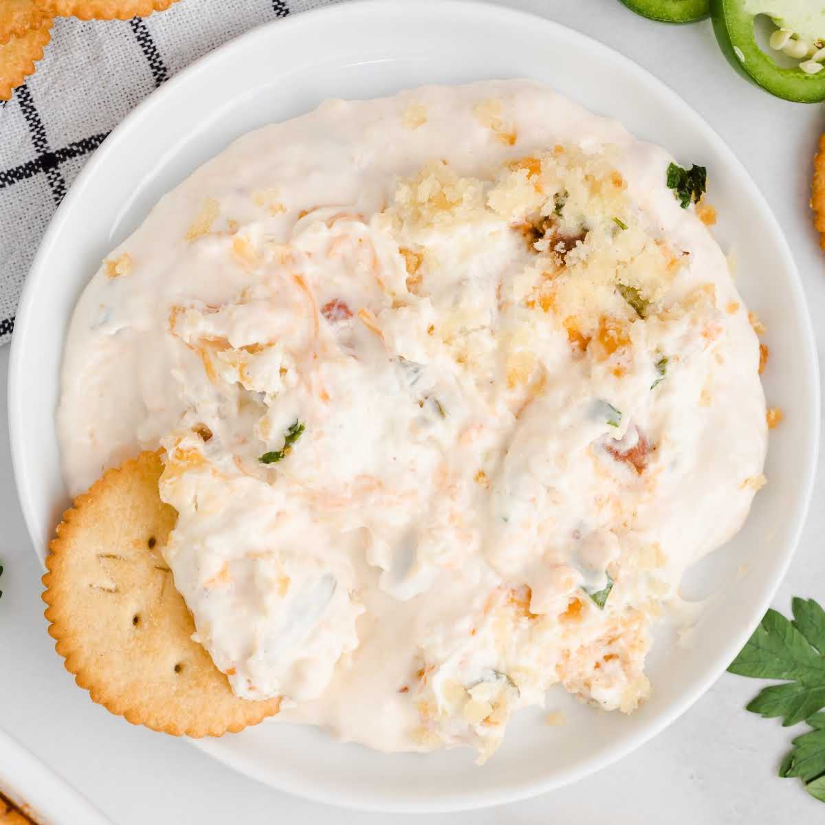close up overhead shot of a bowl of Jalapeno Popper Dip garnished with jalapeños and a ritz cracker dipped into it