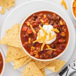 overhead shot of a bowl of Vegetarian Chili topped with sour cream and shredded cheese then placed on a plate of tortilla chips