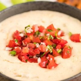 close up shot of a bowl of white queso dip topped with diced tomatoes