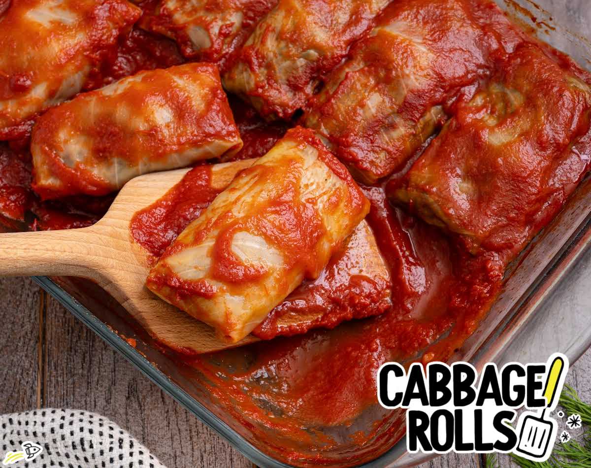 pan of cabbage rolls baked in rich tomato sauce with one roll lifted on a spatula