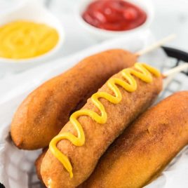 a basket of Homemade Corn Dogs with mustard drizzled on top