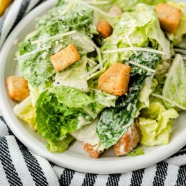 A bowl of salad on a plate, with Caesar salad