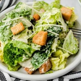 A bowl of salad on a plate, with Caesar salad