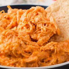 close up shot of a bowl of Crockpot Buffalo Chicken Dip with a tortilla dipped into it