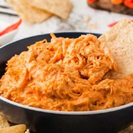 close up shot of a bowl of Crockpot Buffalo Chicken Dip with a tortilla chip dipped into it
