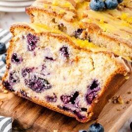close up shot of a loaf of Lemon Blueberry Bread being sliced on a wooden cutting board with blueberries