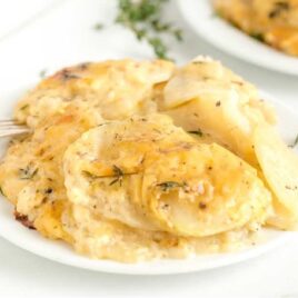 close up shot of a plate of Scalloped Potatoes garnished with fresh thyme