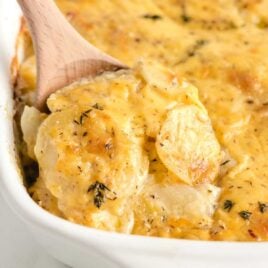 a baking dish of Scalloped Potatoes with a large wooden spoon