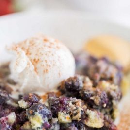 close up shot of blueberry cobbler with a scoop of vanilla ice cream on a plate