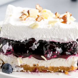 close up shot of a slice of blueberry delight topped with pecans and white chocolate curls on a plate