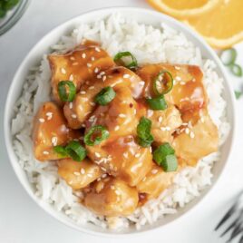 close up overhead shot of a bowl Crockpot Orange Chicken garnished with sesame seeds and green onions then served over white rice