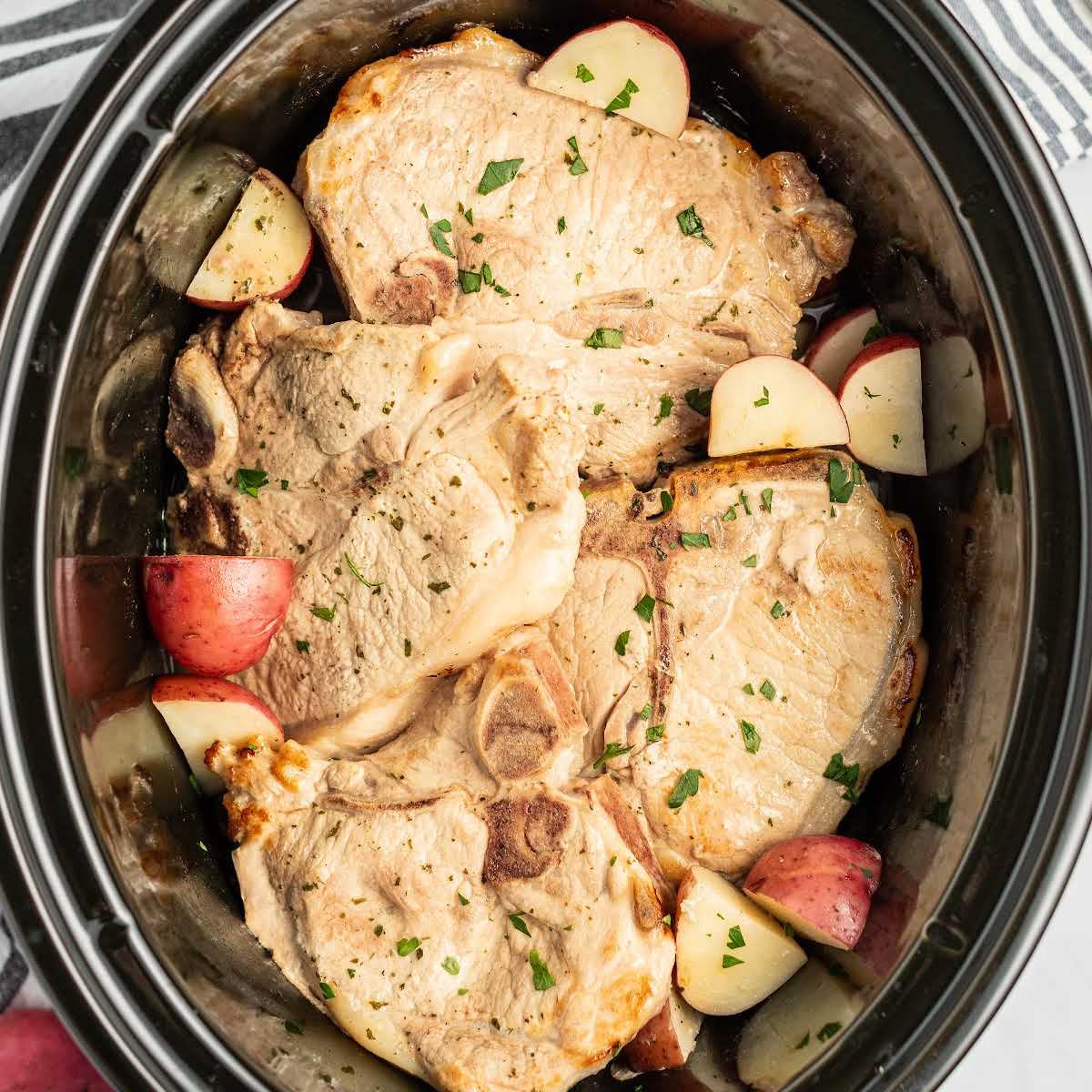 close up shot of a crockpot full of pork chops and diced red potatoes