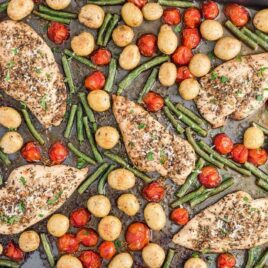 close up overhead shot of a sheet pan full of baked chicken, potatoes, tomatoes, and green beans