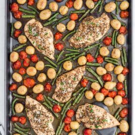 close up overhead shot of a sheet pan full of baked chicken, potatoes, tomatoes, and green beans