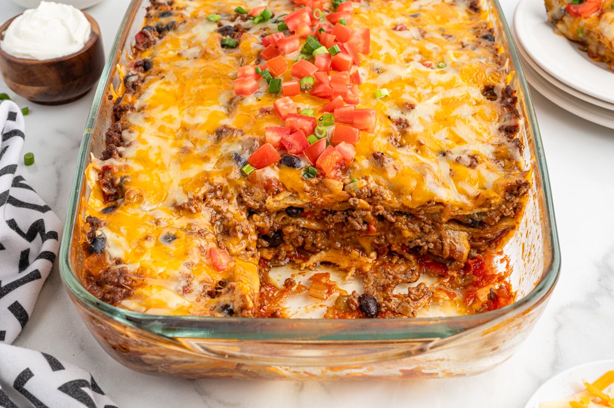 a baking dish of mexican casserole topped with diced tomatoes and green onions
