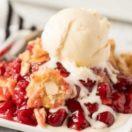 close up shot of a serving of Cherry Dump Cake topped with vanilla ice cream on a plate