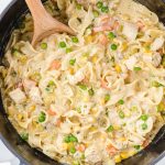 close up overhead shot of Chicken Pot Pie Noodles in a pot with a large wooden spoon