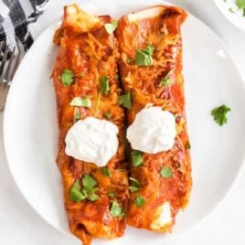overhead shot of a plate of Ground Beef Enchiladas topped with cilantro and sour cream