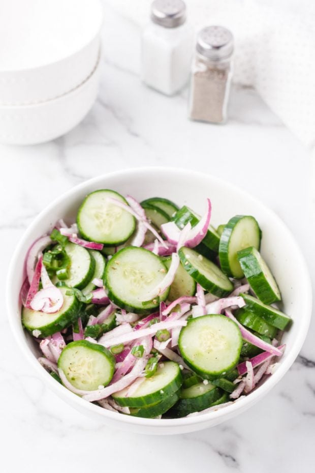 A bowl of food on a plate, with Salad and Cucumber
