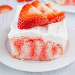 close up shot of a slice of jello poke cake topped with whipped cream and strawberry slices on a plate
