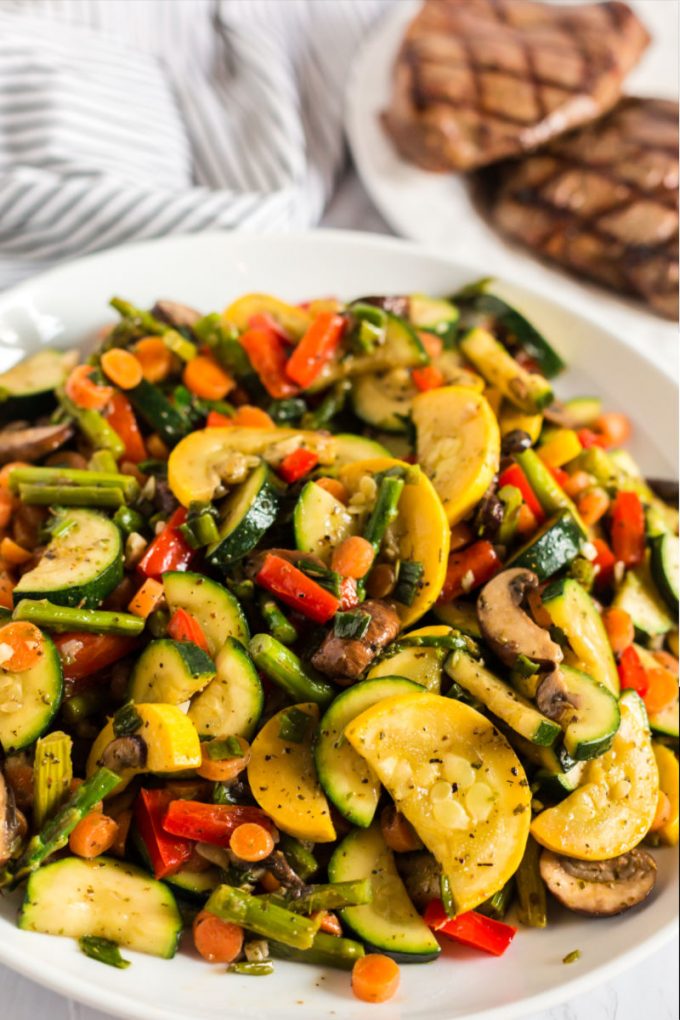 big plate of sauteed vegetables with steak in the background
