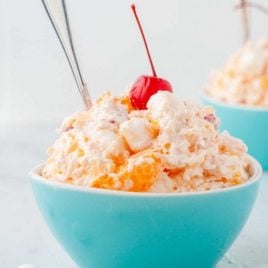 close up shot of Ambrosia Salad topped with a cherry in a baby blue bowl with a spoon