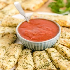 close up shot of Cauliflower Bread Sticks on a plate with a small dipping bowl of marinara sauce