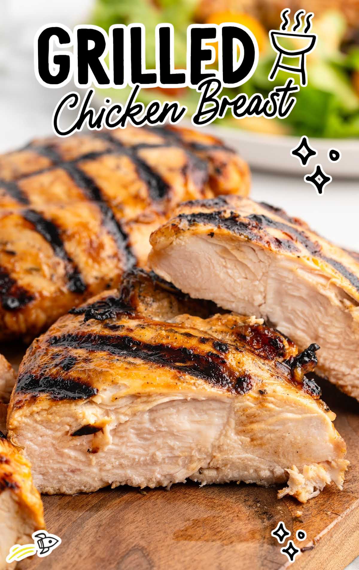 Grilled chicken breasts with golden brown char marks arranged on a board, with one breast sliced open to show juicy interior.