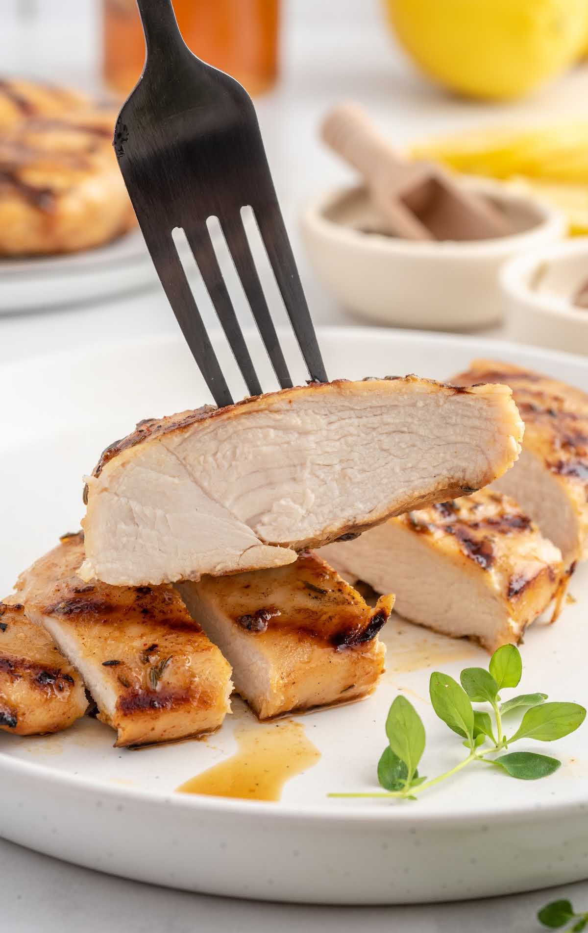 close up shot of slices of Grilled Chicken Breast on a plate with a fork picking one up