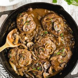overhead shot of Salisbury Steak in a skillet with a wooden spoon