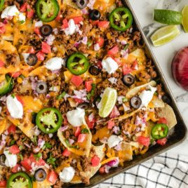 A pizza sitting on top of a table filled with food, with Nachos and Sheet pan