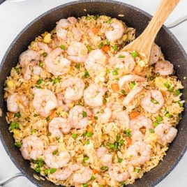 overhead shot of shrimp fried rice garnished with green onions in a pan with a wooden spoon