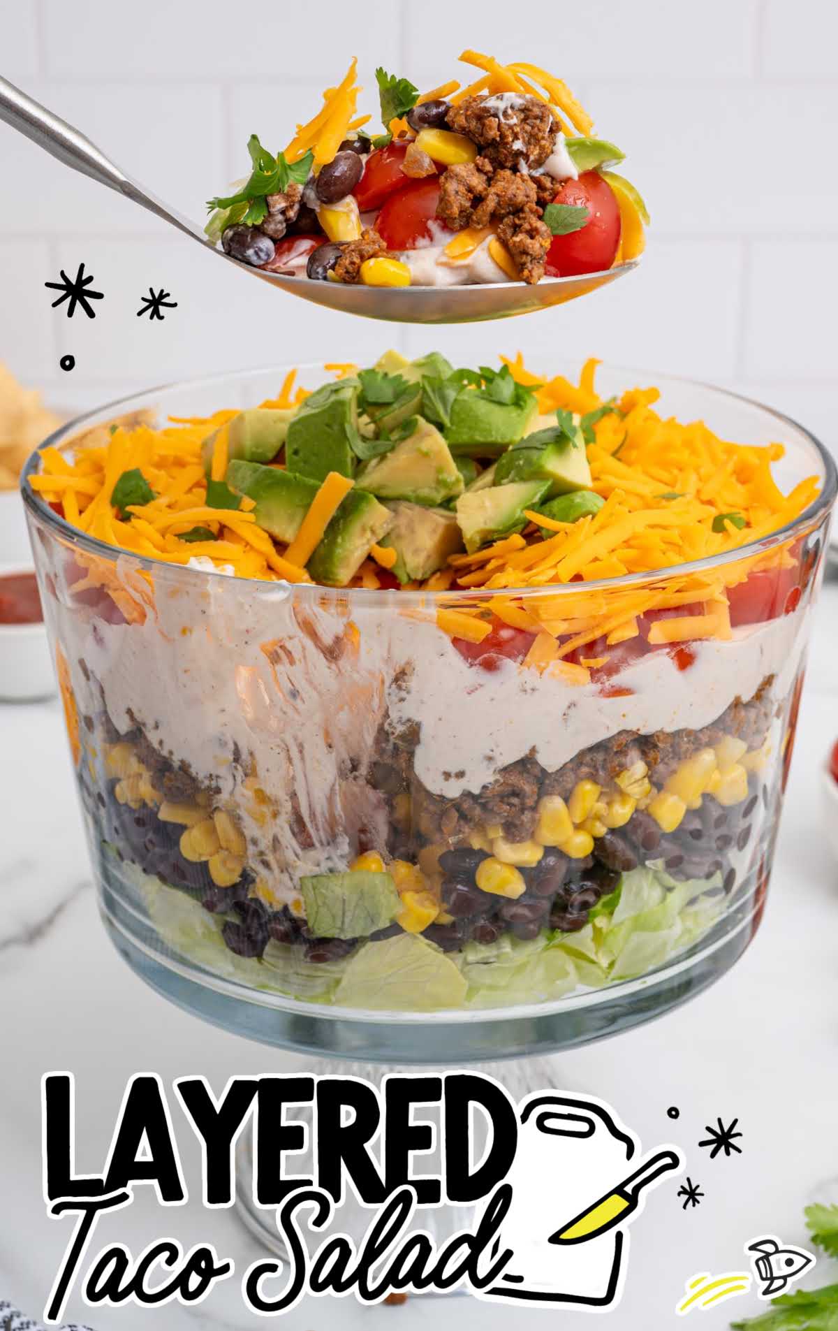 Spoonful of layered taco salad showing ground beef, black beans, corn, cherry tomatoes, cheddar cheese, and creamy taco dressing