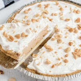 close up shot of No Bake Peanut Butter Pie topped with whipped cream and chopped peanuts with a slice being taken out of it