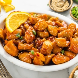 A round oval serving dish full of orange chicken.