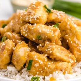 close up shot of a plate of Orange Chicken garnished with sesame seeds and green onions then served over white rice
