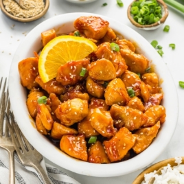 A white serving dish full of orange chicken