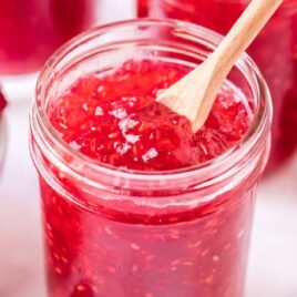 close up shot of a jar of Raspberry Freezer Jam with a bowl of raspberries