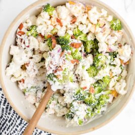 close up overhead shot of a serving bowl of Broccoli Cauliflower Salad with a wooden spoon