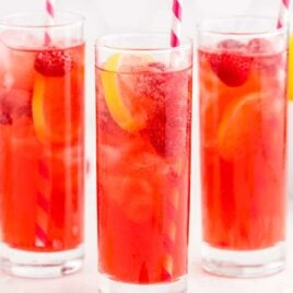 close up shot of glasses of Raspberry Iced Tea garnished with lemon slices and raspberries and served with a straw