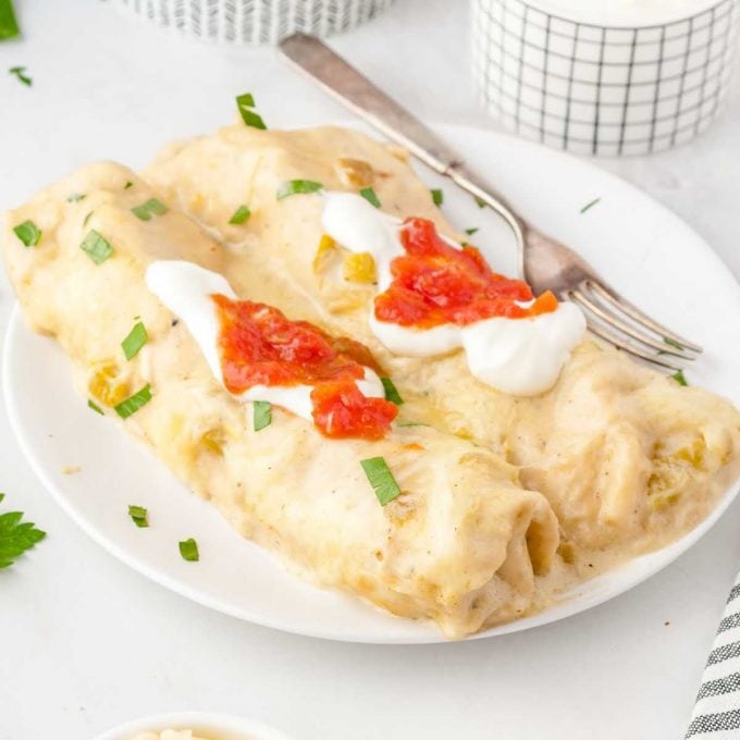 close up shot of a plate of White Chicken Enchiladas topped with sour cream and salsa then garnished with cilantro