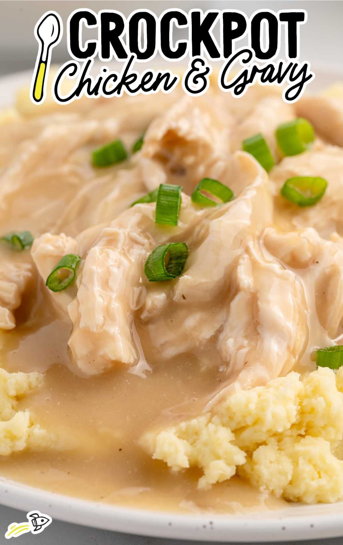 Close-up of crockpot chicken and gravy served over mashed potatoes with green onions.